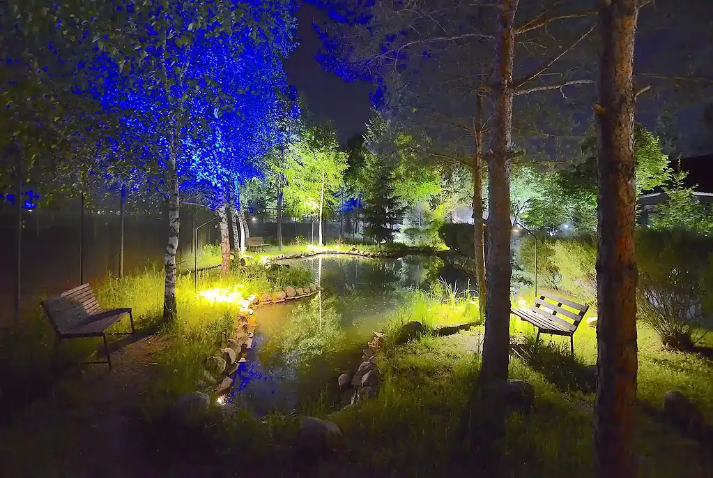 Уютный ночной вид на освещённый сад с скамейками и озером в VE Art Resort в Подмосковье. Идеальное место для отдыха на природе с красивой подсветкой и спокойной атмосферой.