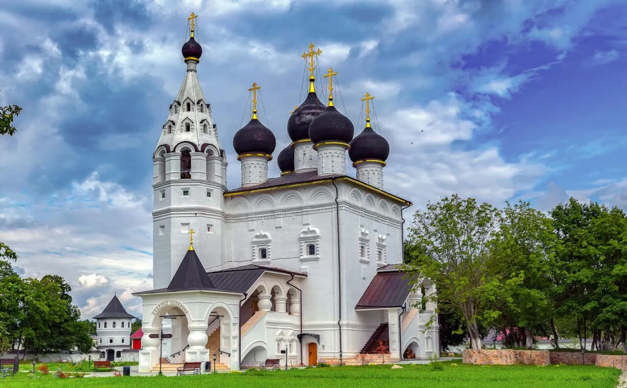 Уникальный российский храм с традиционными черными куполами на фоне зелени и голубого неба.