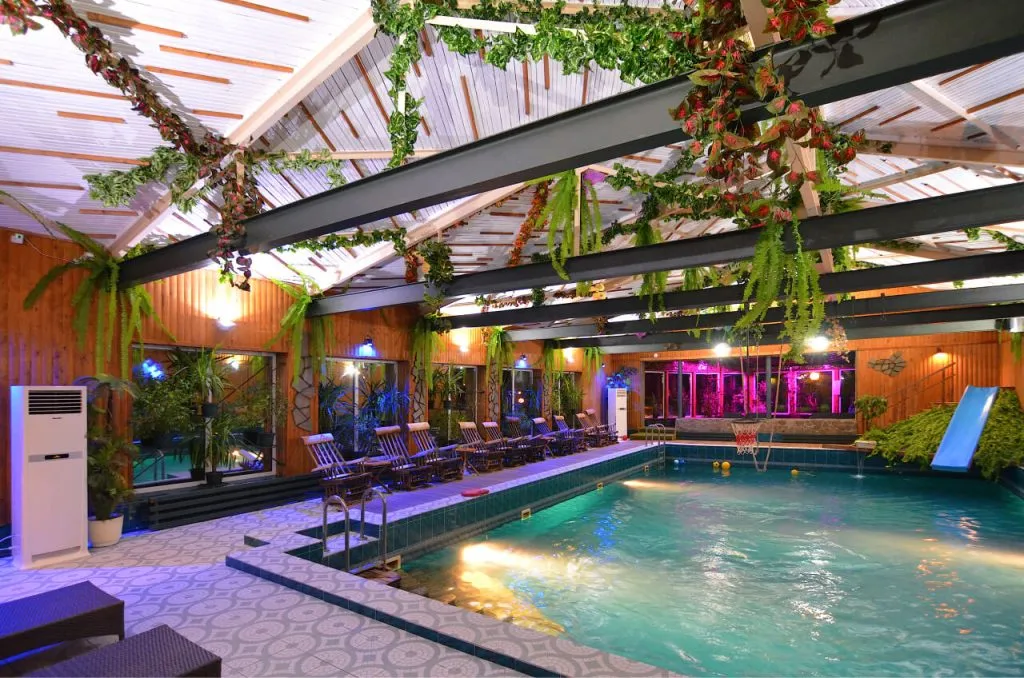 уютный бассейн внутри отеля VE Art Resort с теплой водой и ярким освещением, окруженный зеленью и деревянным интерьером, создающим уютную атмосферу для отдыха и релаксации.