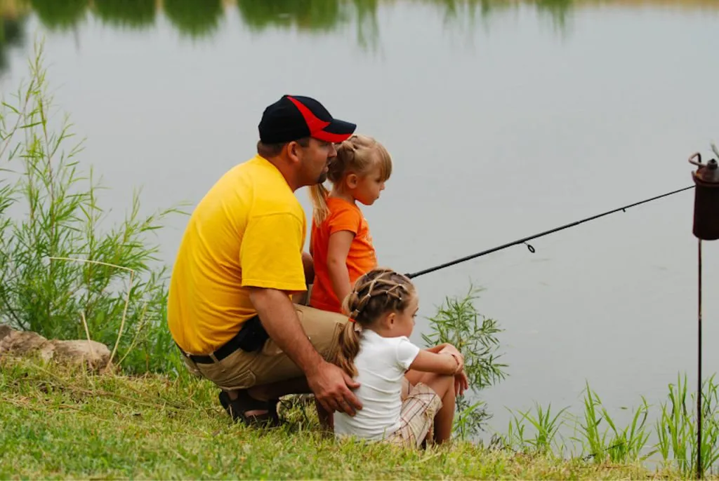 Родители с детьми рыбачат у воды в природном парке подмосковья. Семья наслаждается отдыхом на природе, ловит рыбу, окружена зеленью и спокойствием водоема. Perfect для семейного отдыха.