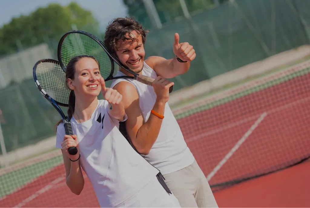 Улыбающиеся молодые люди с ракетками на теннисном корте, наслаждающиеся активным отдыхом в подмосковье.