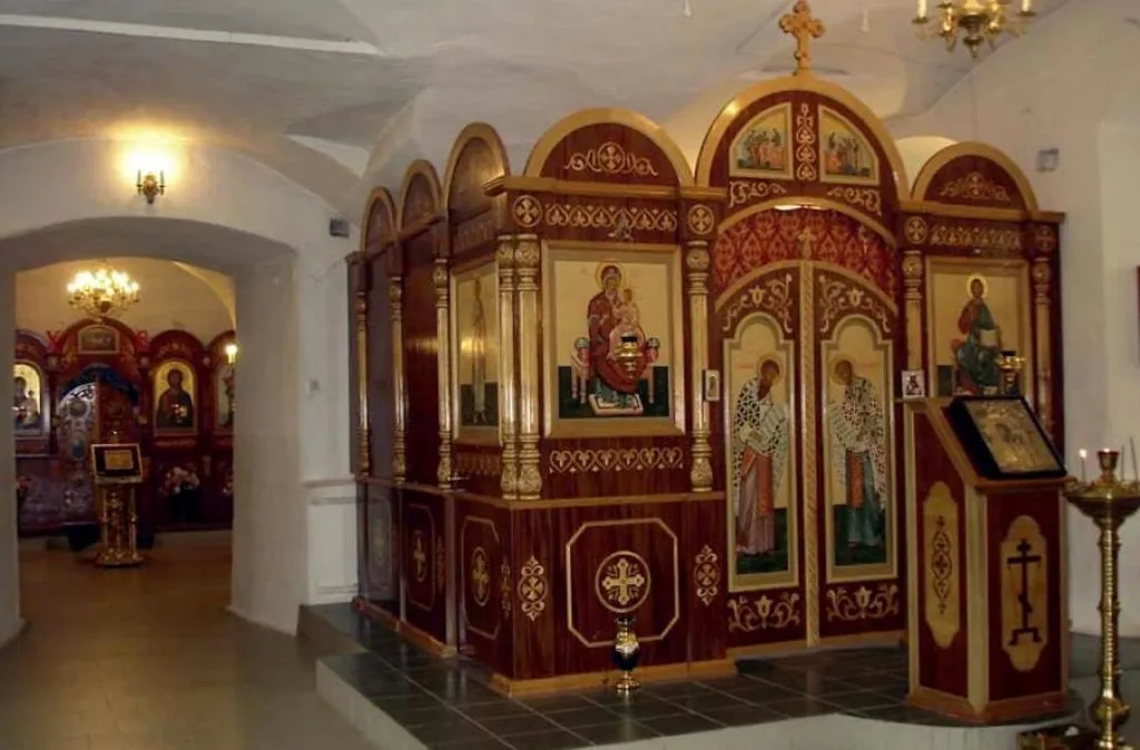 Кнопка, иконостас в православной церкви, выполненные из дерева с золотой отделкой и религиозными изображениями внутри. Внутреннее пространство церкви с мягким освещением и уютной атмосферой.