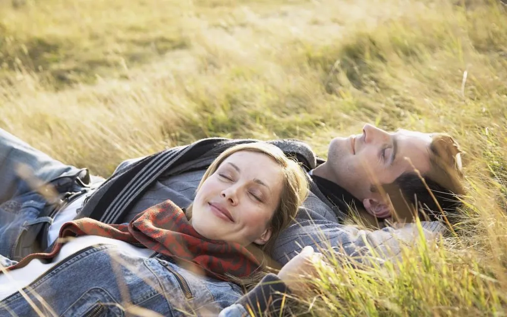 Отдых в природной обстановке на лугу, пара лежит на траве, наслаждаясь солнечным днем. Передают атмосферу релакса, спокойствия и гармонии, характерную для отдыха в ВЕ Art Resort в Подмосковье.