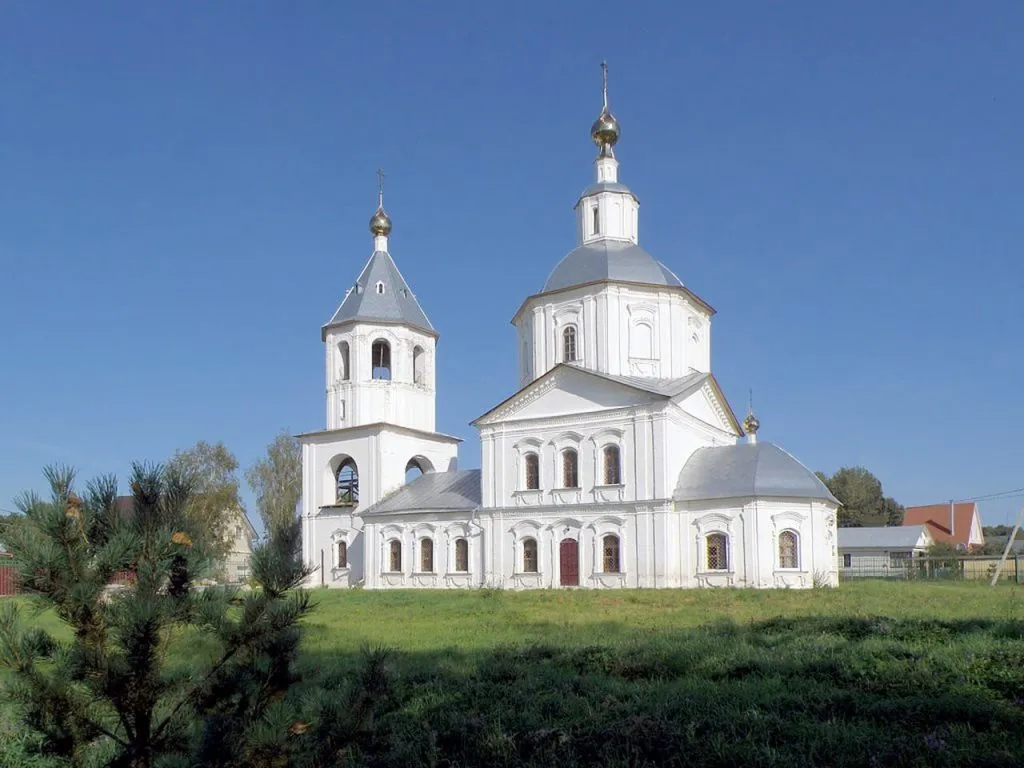 старая белая церковь с золотыми куполами на зеленом лугу на фоне ясного голубого неба.