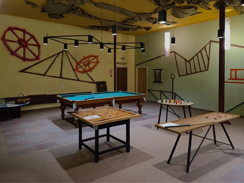 Римский интерьер игрового зала с бильярдным столом, настольными играми и декоративными элементами в стиле модерн. Мягкое освещение создает уютную атмосферу для отдыха и развлечений.