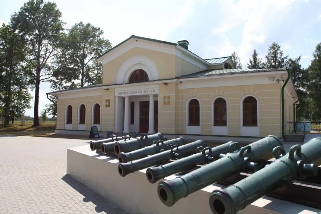 Историческое здание музея с пушками на переднем плане, окружённое деревьями и ясным небом. Добро пожаловать в музей Бородинской битвы в Подмосковье. Отличное место для экскурсии и прогулки.