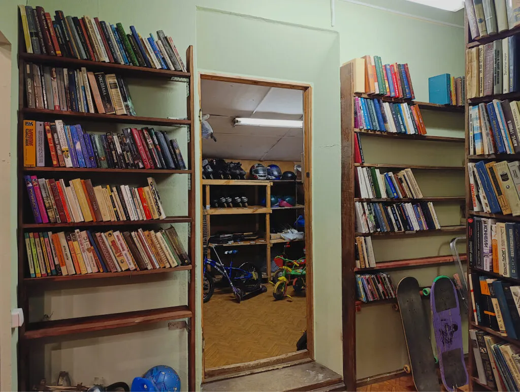 Книги на полках в библиотеке или игровой комнате, множество литературных томов и спортивного инвентаря, создающие уютную атмосферу для отдыха и развлечений.