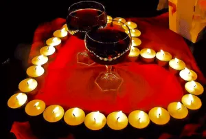 роспись на столе с двумя бокалами красного вина, окруженная свечами в форме сердечка, романтическая атмосфера, уют и теплая встреча, вечерние развлечения и романтический ужин ВЭ Арт Ресорт.