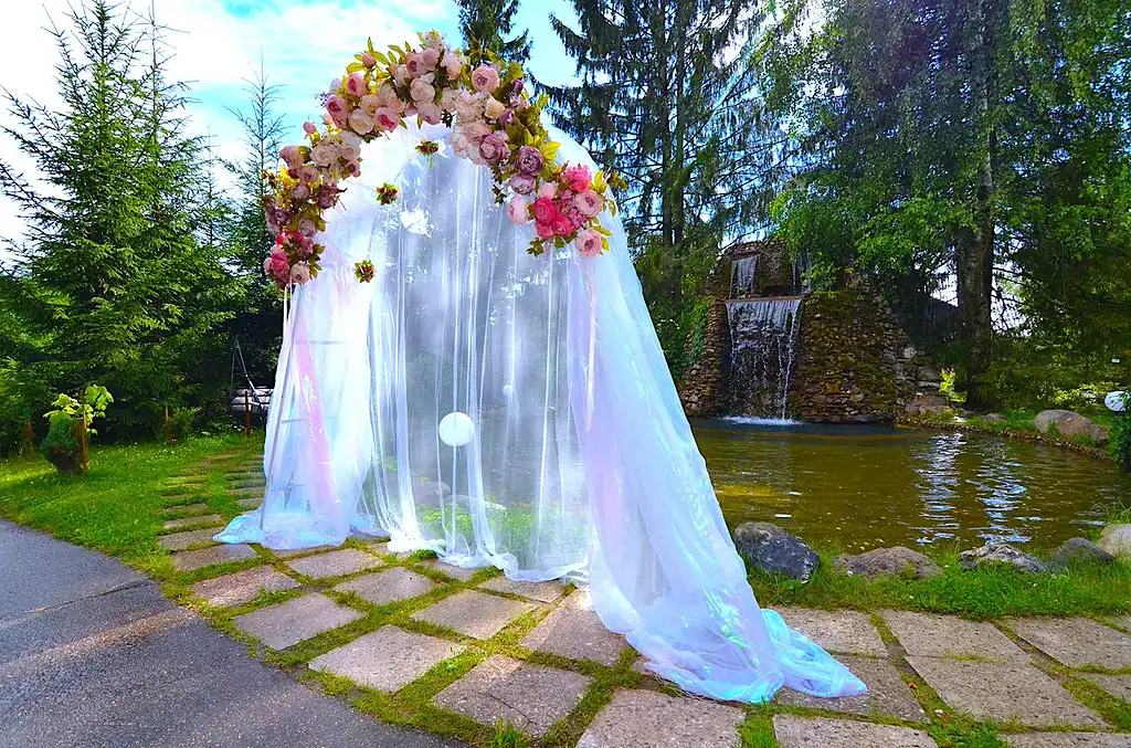 Элемент оформления свадьбы на природе с цветочной аркой и водопадом возле пруда в загородном отеле VE Art Resort. Идеально подходит для романтических церемоний на свежем воздухе.