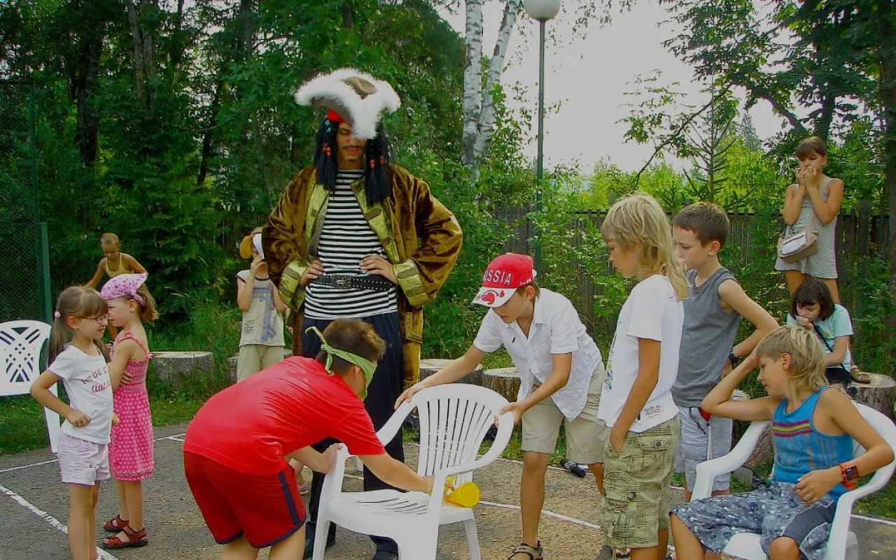 игра детей в лесу на празднике с куклой и аниматором на фоне зелени и деревьев.