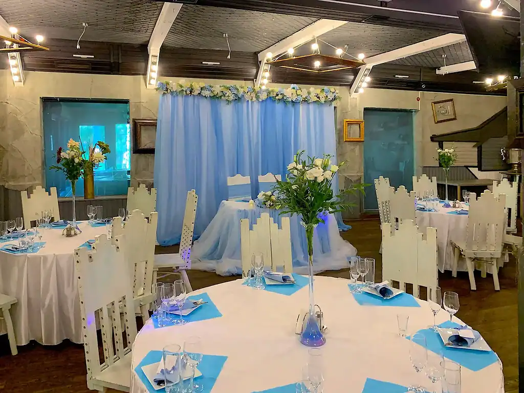 Современное зала для свадебной церемонии в VE Art Resort с белыми столами, голубыми салфетками и высокими вазами с белыми цветами, уютная атмосфера для праздника в Подмосковье.