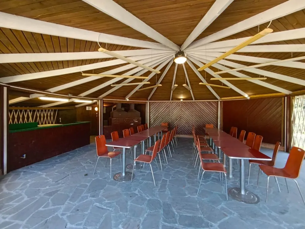 Уютный зал с деревянной отделкой, круглый потолочный вентилятор и длинные столы с красными стульями, созданный для отдыха или мероприятий в SV Art Resort под Москвой.