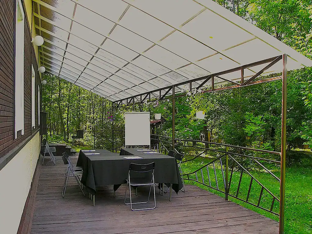 Уютная открытая беседка на деревянной террасе с зеленым фоном и столом, накрытым черной скатертью, предназначена для проведения мероприятий на свежем воздухе в ВЕ Art Resort.