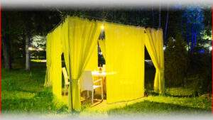 Уличная зона отдыха с желтыми шторами и столом в зеленом парке, уютное место для отдыха и встреч на природе.